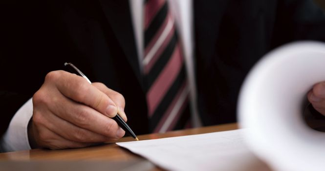 Hombre trajeado firmando papeles